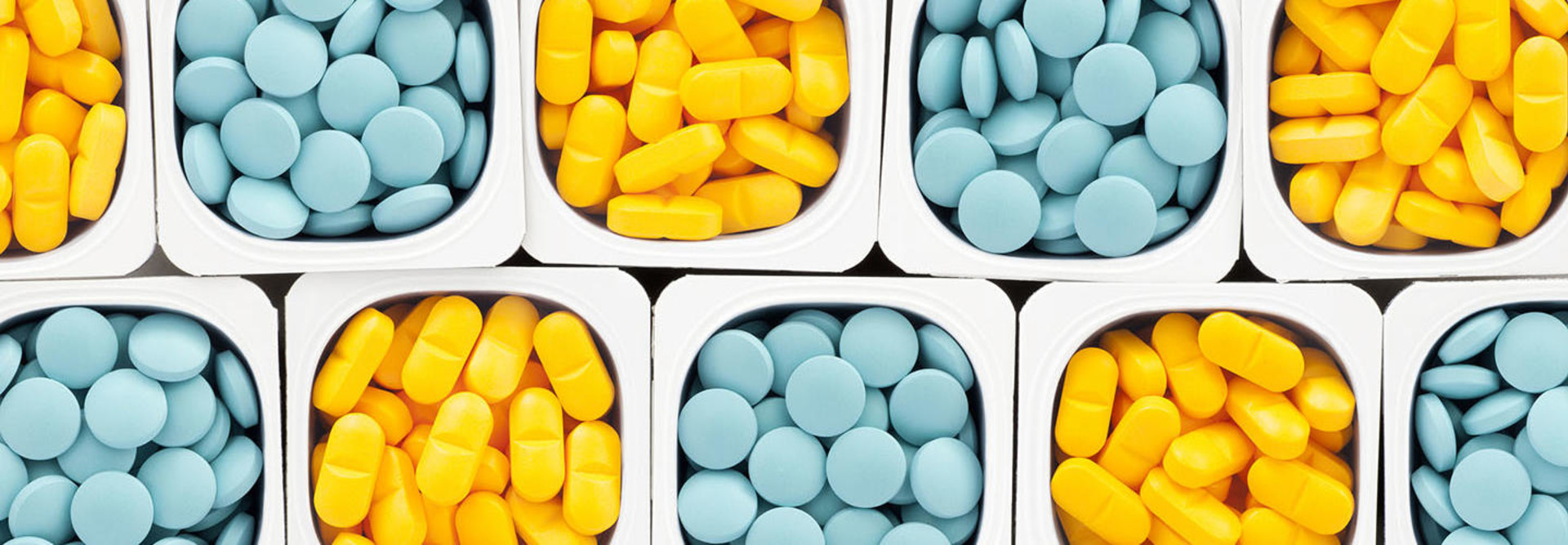 Top view of lots of pills held in plastic containers in a crisscross pattern