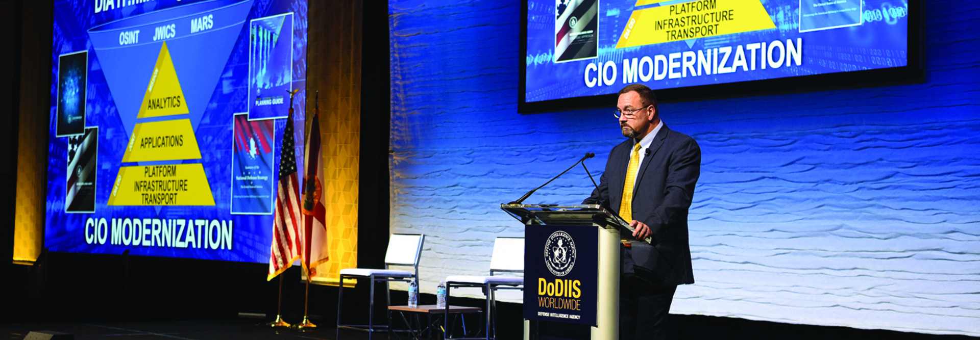 Man at podium with slides of pyramids with words