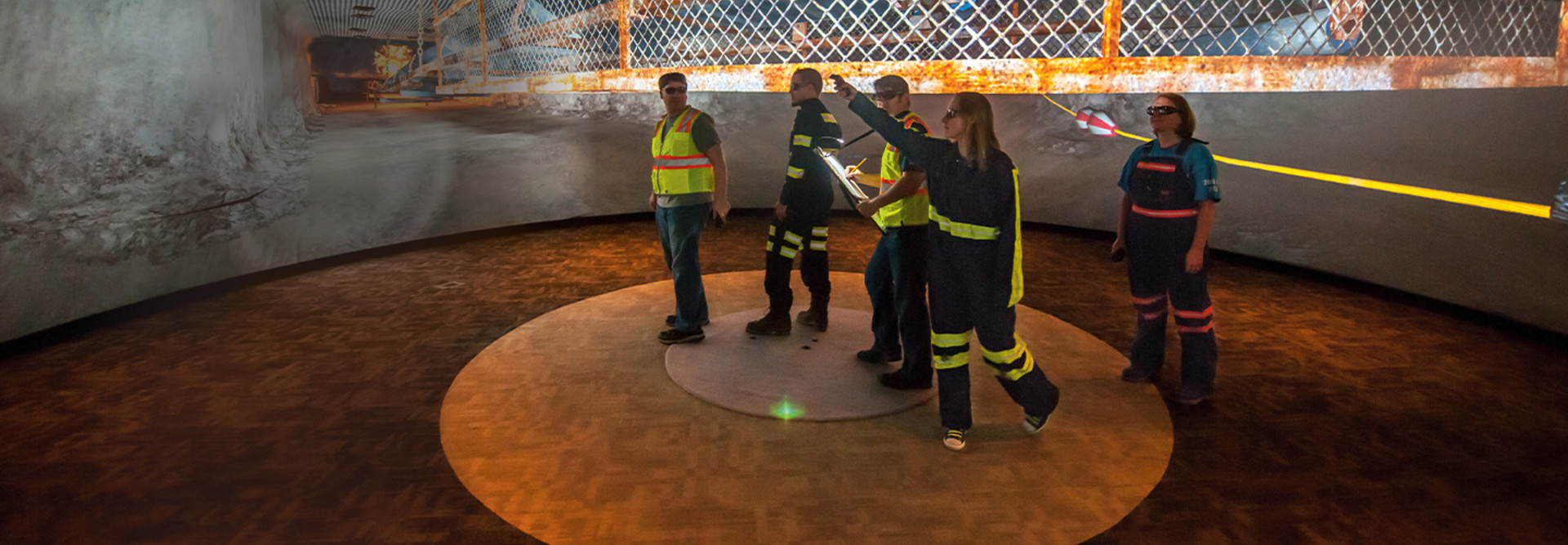 Research Lead Jennica Bellanca guides NIOSH workers through a virtual scenario on how to safely escape from a mine emergency. Each worker has a controller to operate the VR; the captain’s navigates them through the exercise. At left, what the 360-degree space looks like without VR.