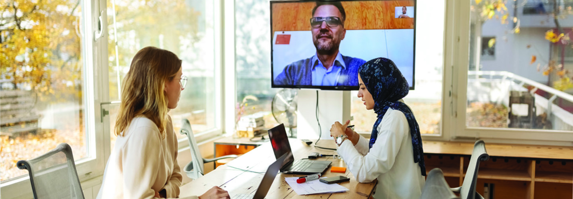 blonde woman and woman in scarf in a meeting with a guy on a screen