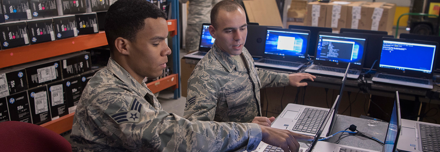 Senior Airmen Jonathon Clayton, left, and Dylan Bender, 21st Communication Squadron client systems technicians, work together to bring new Windows 10 laptops into compliance with Air Force standards at Peterson Air Force Base, Colo., March 22, 2017. 