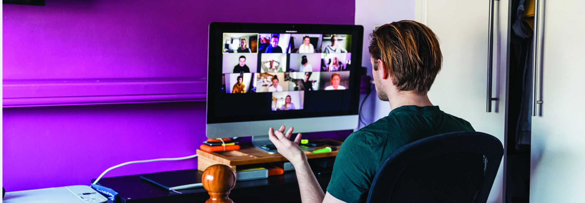 man sitting at computer in a home office with a purple wall and an open closet door