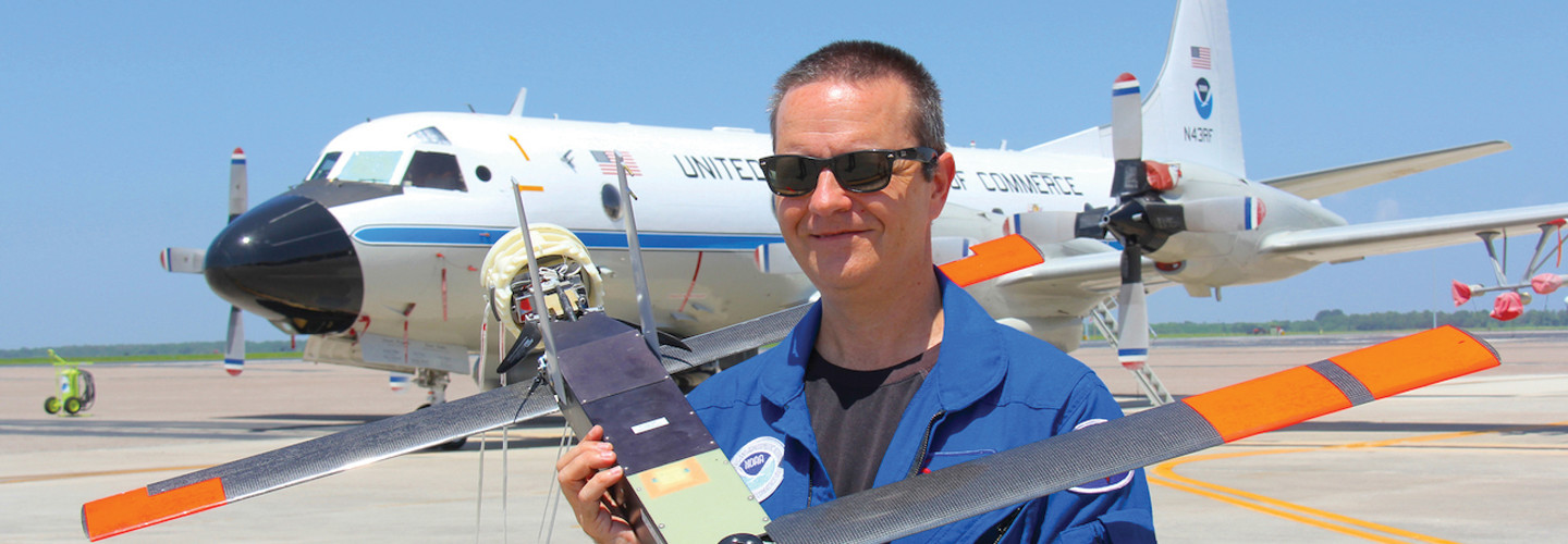 Joe Cione holding a drone and standing in front of a plane