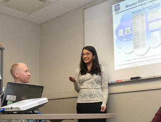 Ammu Irivinti, MITRE senior systems engineer, standing, speaks with, from left to right, Capt. Devon Messecar, System Engineering Integration Contract II program manager, Steve Harrison, MITRE Advanced Development lead, and Dave Parker, deputy PM, at Hanscom Air Force Base, Mass., on Nov. 13, 2015, regarding the use of Hanscom MilCloud to improve mission planning.