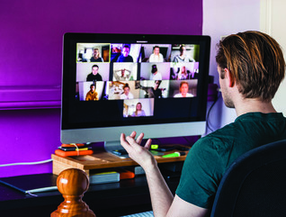 man sitting at computer in a home office with a purple wall and an open closet door