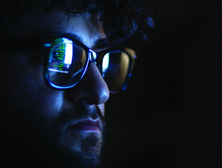 Computer code reflected on the glasses on a man's face