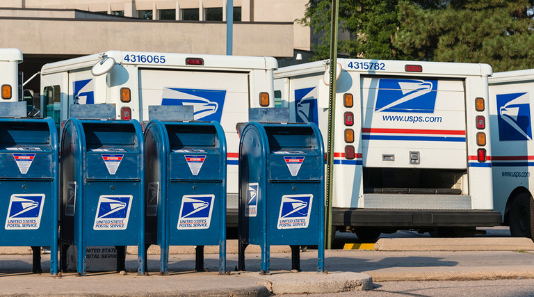 Mailboxes and USPS mail trucks lined up in a parking lot 