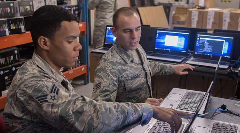 Senior Airmen Jonathon Clayton, left, and Dylan Bender, 21st Communication Squadron client systems technicians, work together to bring new Windows 10 laptops into compliance with Air Force standards at Peterson Air Force Base, Colo., March 22, 2017. 