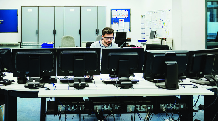 Man sitting behind an array of computer screens