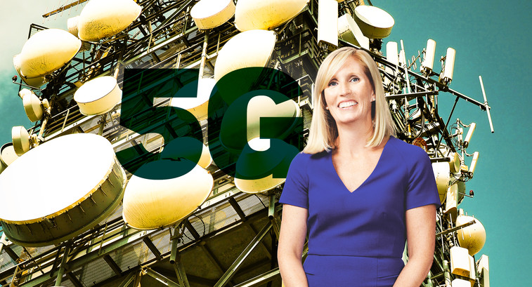 blonde woman in blue dress standing in front of a 5G tower